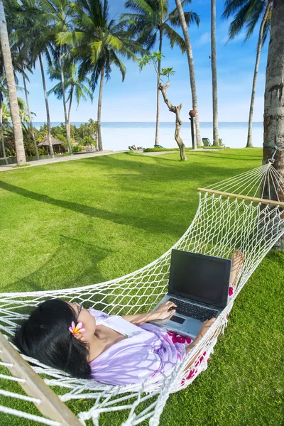 Ισομετρική γραφήματα在海滩的亚洲女孩工作在吊床上用的笔记本电脑 — 图库照片