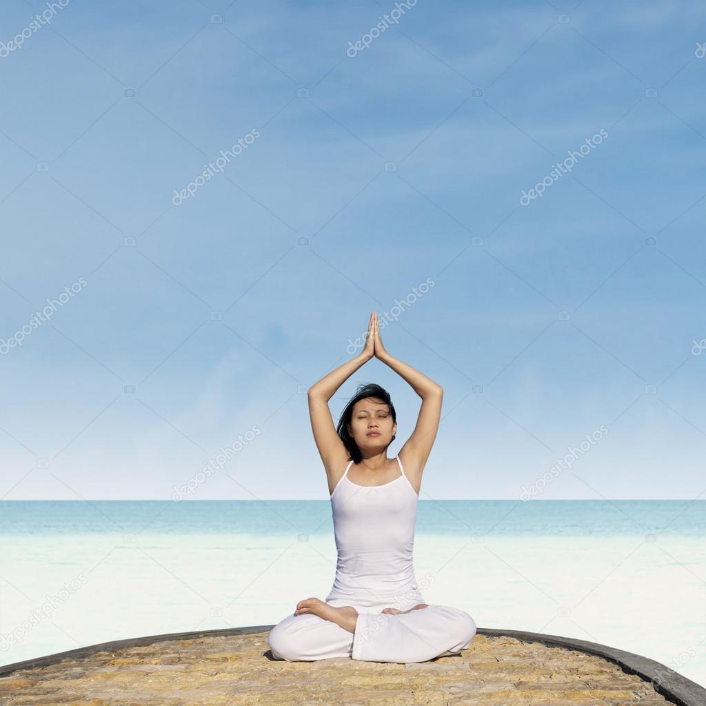 Asian woman practicing yoga at beach