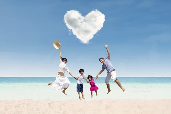 Feliz família pulando sob nuvem de amor na praia — Fotografia de Stock