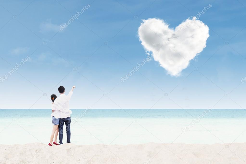 Couple honeymoon at beach under heart cloud