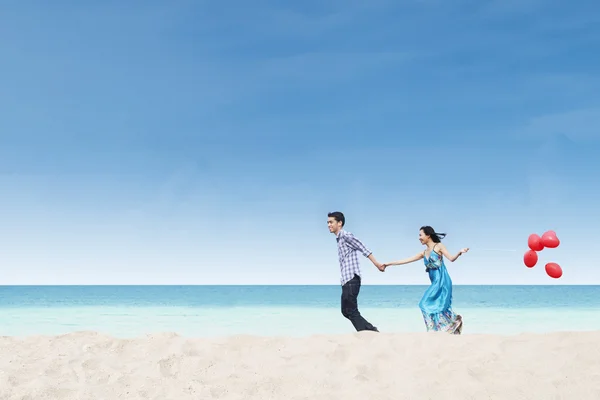 Laufendes Paar am Strand mit Luftballons — Stockfoto