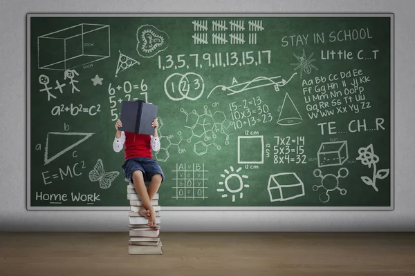 Ragazzo lettura libro in classe seduto su pila di libri — Foto Stock