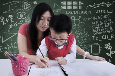 çekici öğretmen sınıfta yazmak için bir çocuk yardım