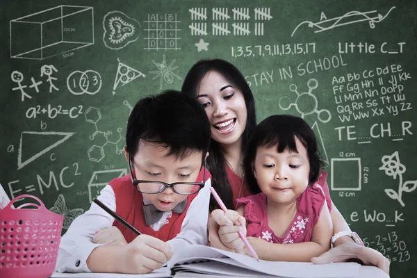 Bela professora ver crianças escrevendo em sala de aula — Fotografia de Stock