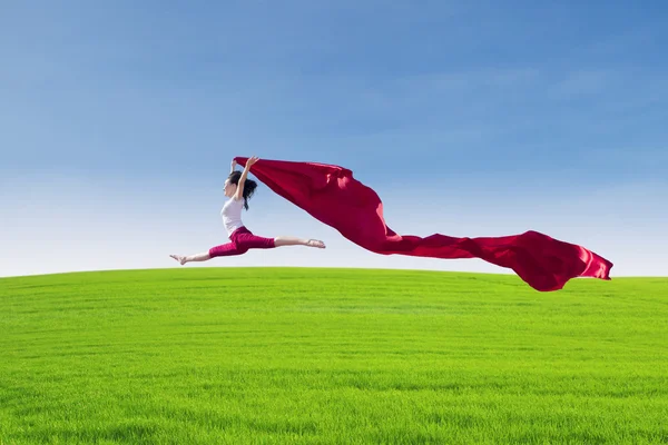 Beautiful female jumping with red scarf on field — Stock Photo, Image