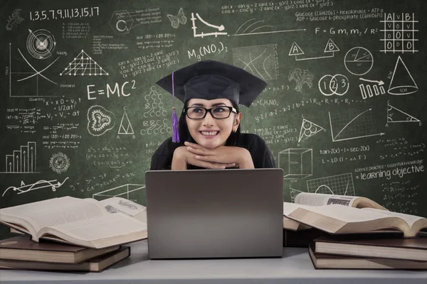 Feliz mujer graduada pensando en usar el portátil en clase — Foto de Stock