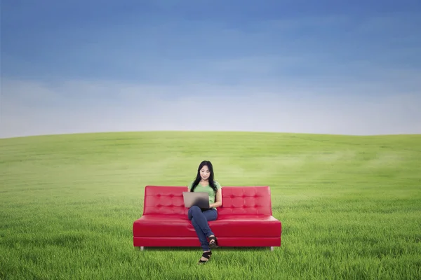 Привлекательная женщина работает на красном диване на открытом воздухе — стоковое фото