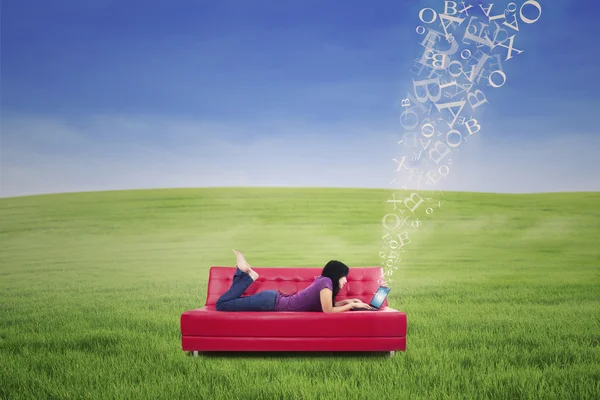 Привлекательная женщина лежит на красном диване и печатает электронную почту на открытом воздухе — стоковое фото