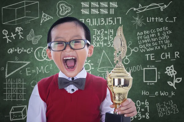 Excitado estudante menino segurando troféu na classe — Fotografia de Stock