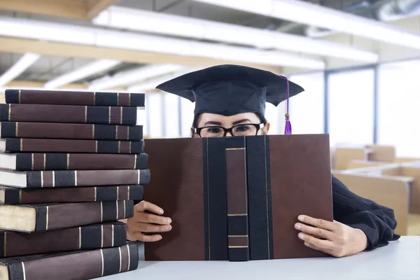 Young female bachelor covering her face with book in library — Stock Photo, Image