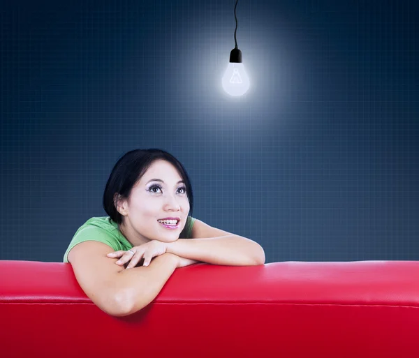 Asiatin schaut Lampe auf rotem Sofa an — Stockfoto
