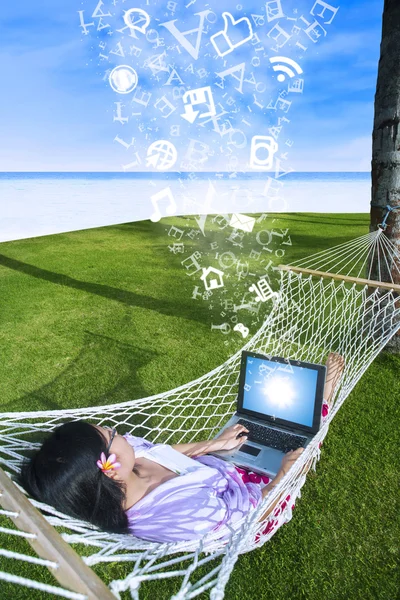 Aziatische vrouw met behulp van laptop op hangmat op strand — Stockfoto