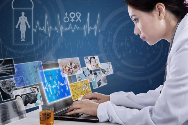 Busy doctor typing on laptop with digital pictures — Stock Photo, Image