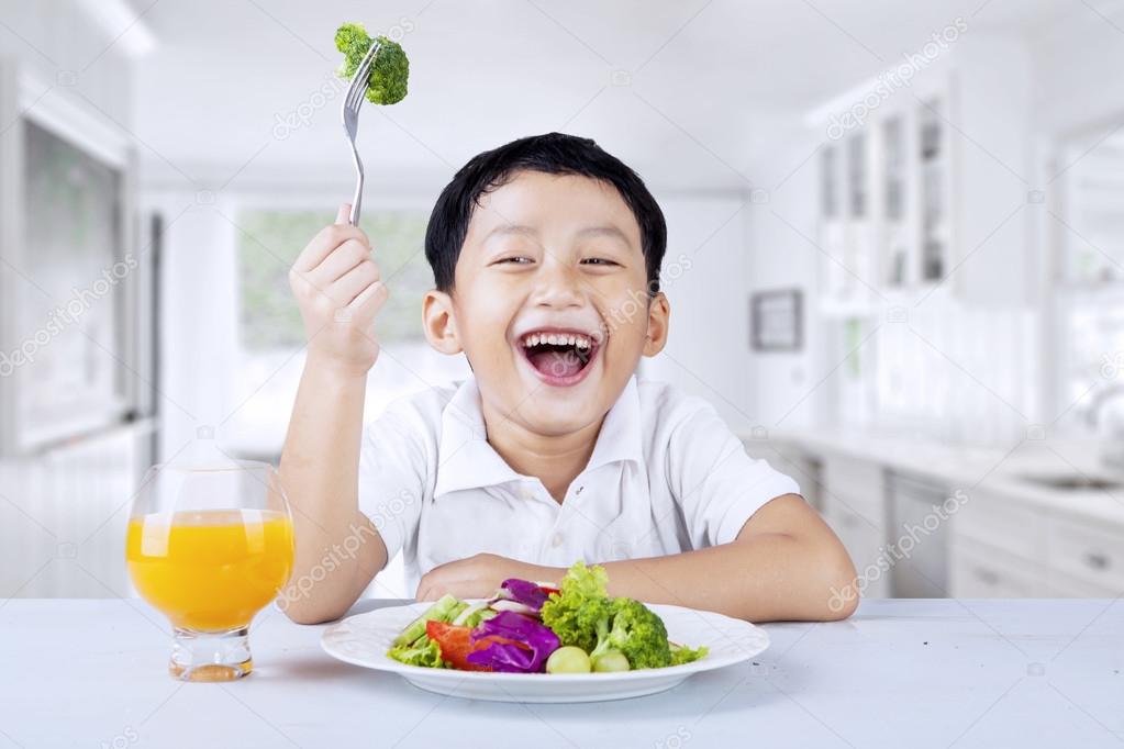 A boy eats vegetable salad in the kitchen