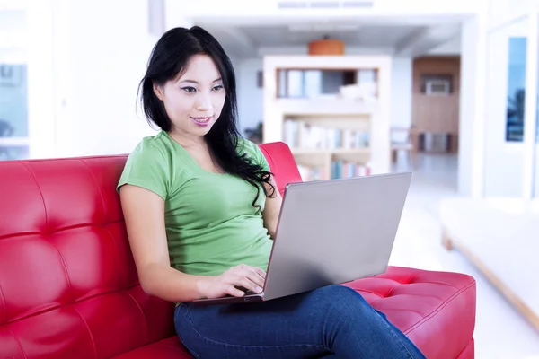 Aantrekkelijke vrouw typen op rode sofa thuis — Stockfoto