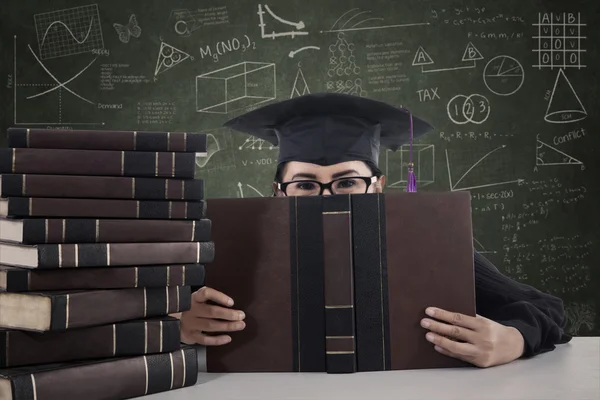 Asian female graduate peeking from behind a book — Stock Photo, Image
