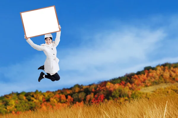 Young woman jumping and holding blank board — Stock Photo, Image