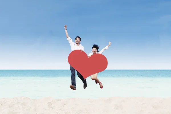 Азиатская пара прыгает на пляже с карточкой сердца — стоковое фото
