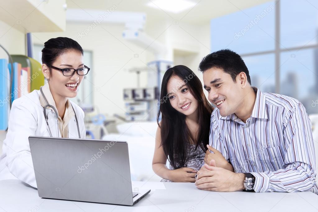 Female doctor looking a laptop with couple in clinic