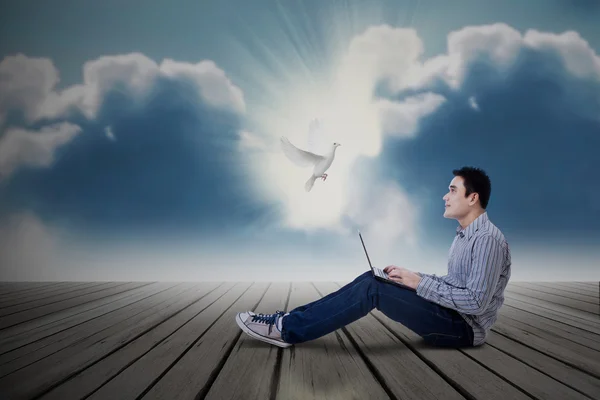 Asian male student looking at dove with laptop — Stock Photo, Image