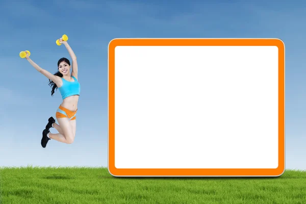 Happy fitness woman jumps next to blank board — Stock Photo, Image