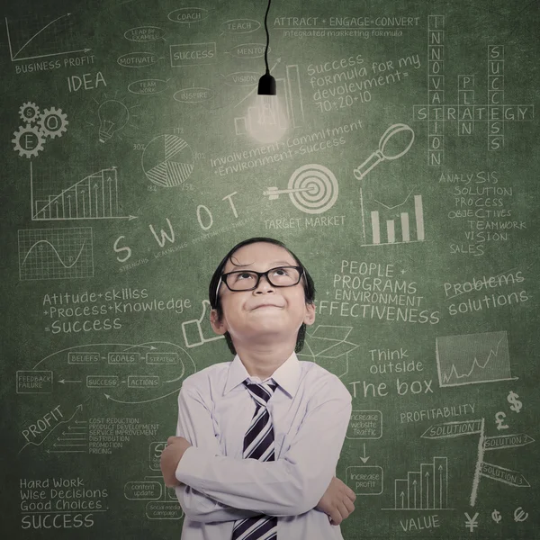 Little businessman looking at lit bulb in class — Stock Photo, Image