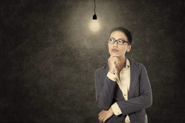 Businesswoman thinking under lit bulb — Stock Photo, Image