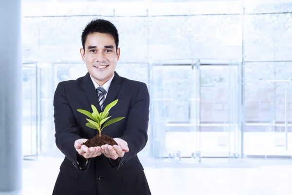 Lachende zakenman bezit een plant — Stockfoto