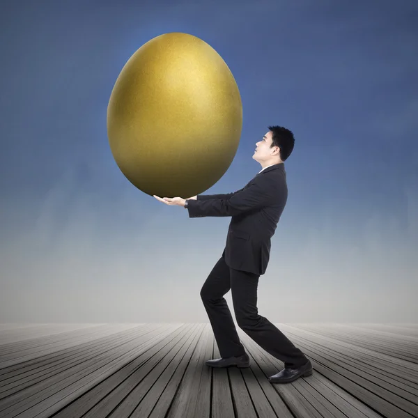 Businessman holding big golden egg — Stock Photo, Image