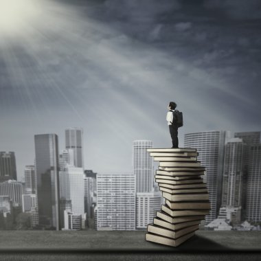 bir kitap yığını üzerinde duran çocuk
