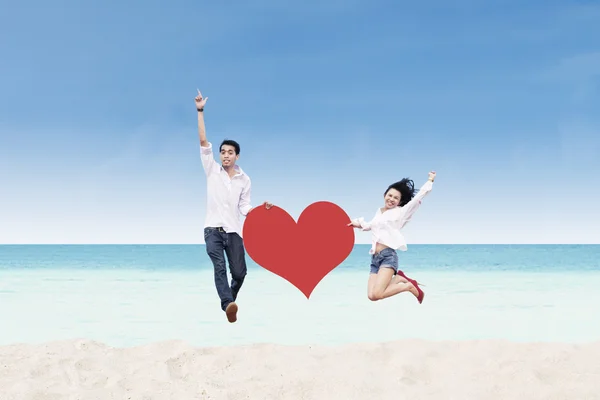 Asiatisches Paar springt mit Herzkarte am Strand — Stockfoto