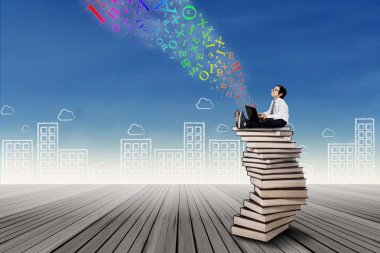 dizüstü bilgisayar ile kitap yığını üzerinde oturan çocuk