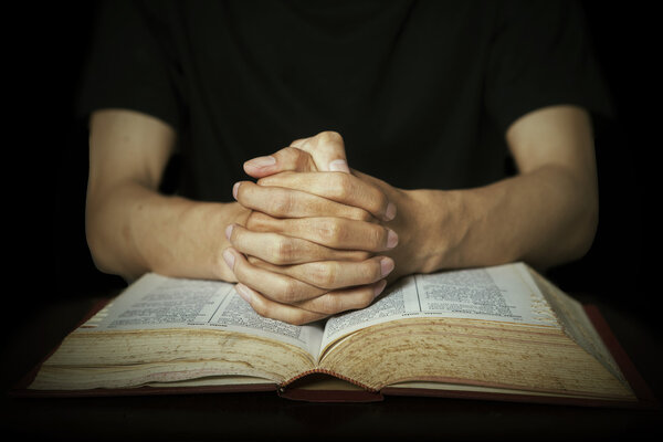 Hands praying on bible