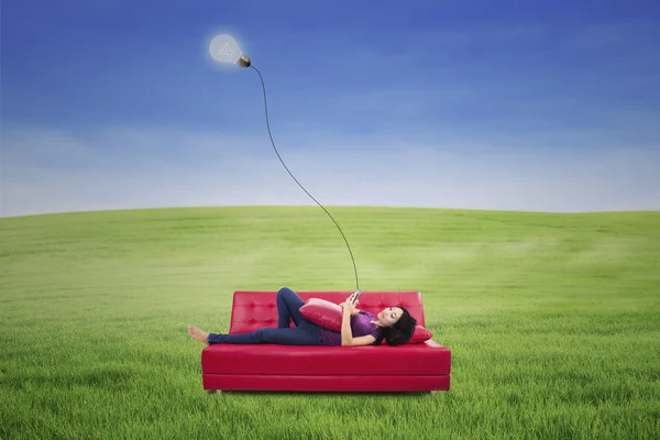 Mulher asiática deitada no sofá vermelho com touchpad sob lâmpada ao ar livre — Fotografia de Stock