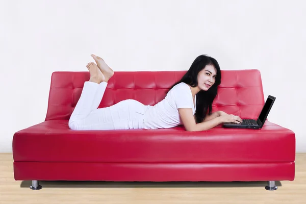 Mujer atractiva usando el ordenador portátil en un sofá — Foto de Stock