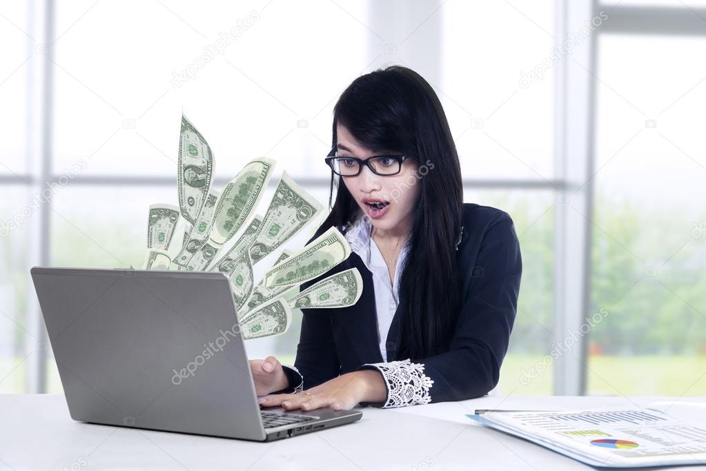 Shocked businesswoman looking money at laptop