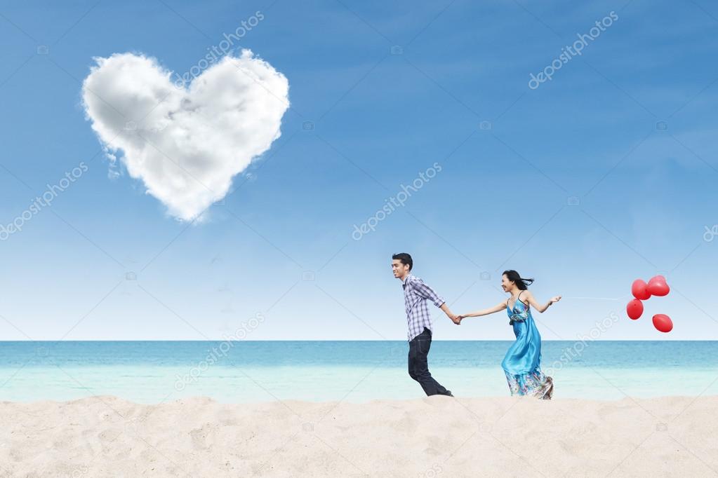 Running couple at beach under heart cloud