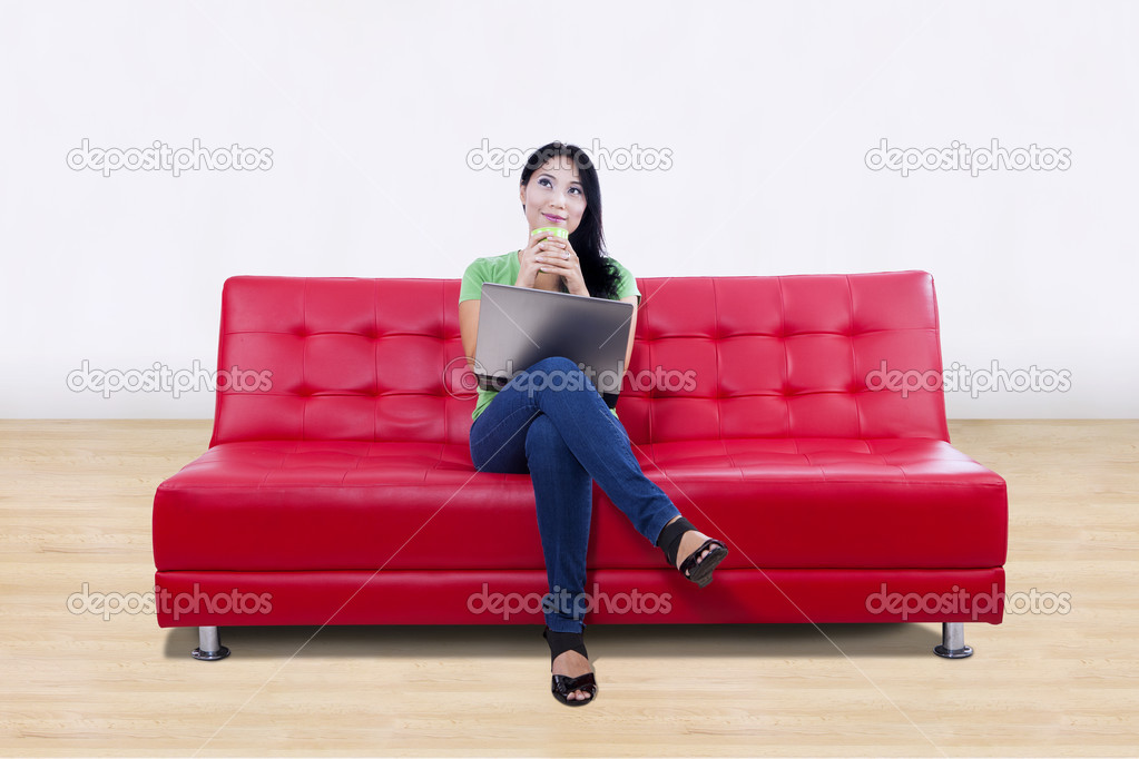 Asian female thinking on red sofa with laptop at home