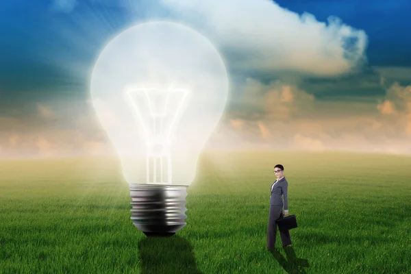Businesswoman with bulb on the meadow — Stock Photo, Image