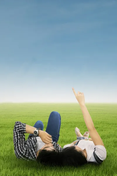 Couple lying on grass pointing at sky — Stock Photo, Image