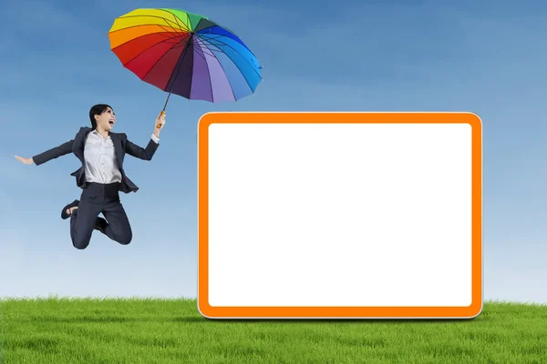 Businesswoman with umbrella jumping on the meadow — Stock Photo, Image