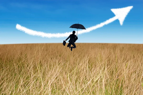 Businesswoman jumping holding umbrella in field — Stock Photo, Image