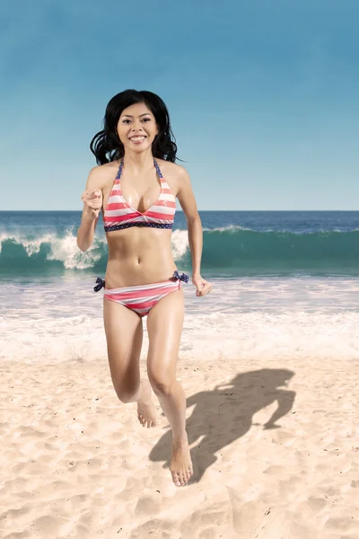 Vrolijke vrouw in bikini joggen op strand — Stockfoto