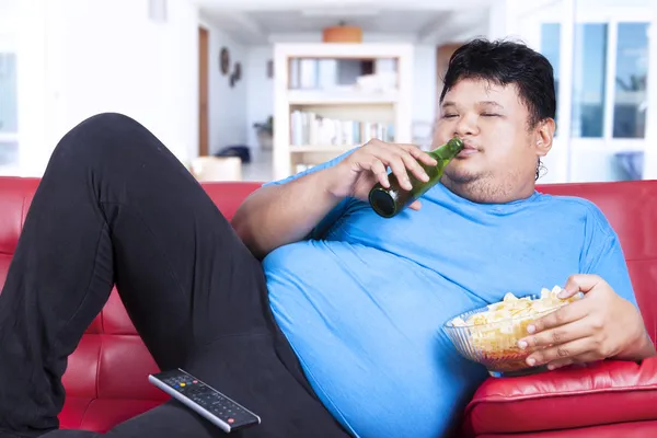Tlustý muž pít pivo a jíst svačinu — Stock fotografie