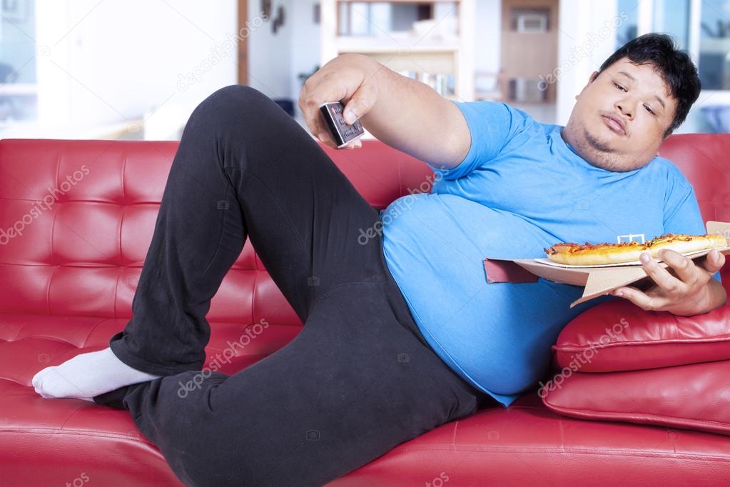 Obese man holds pizza and remote