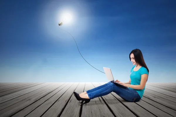 Female student typing on laptop with lit bulb — Stock Photo, Image