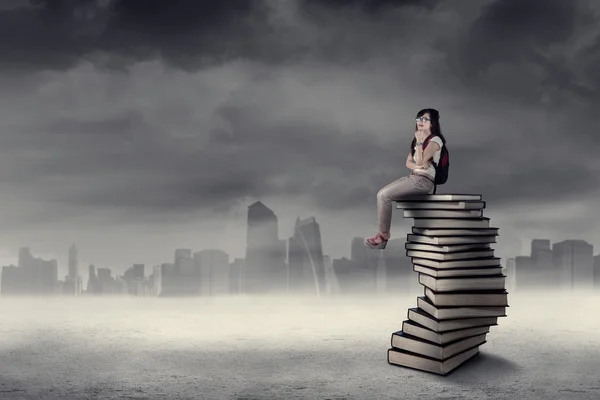 Thoughtful student sitting on books — Stock Photo, Image