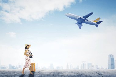 Uçak arka planında yürürken bavul ve pasaport taşıyan bir kadın turist.