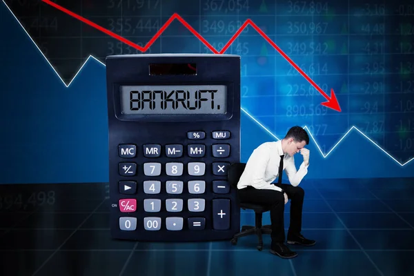 為替レートの下落に近い計算機に破産した言葉で座っているストレスのあるビジネスマン背景 — ストック写真