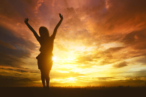 Силуэт деловой женщины, выражающей успех, поднимая руки, стоя на драматическом фоне неба
